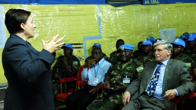 Shelly Whitman debout devant Roméo Dallaire, assis au centre de militaires rwandais en uniforme. Shelly Whitman debout devant Roméo Dallaire, assis au centre de militaires rwandais en uniforme.