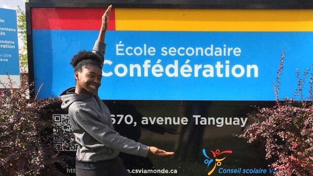 Photo de Sherna devant le panneau de l'école Photo de Sherna devant le panneau de l'école