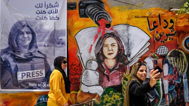 Une Palestinienne se photographie devant une murale montrant un fusil duquel sort du sang au-dessus de la journaliste. 
