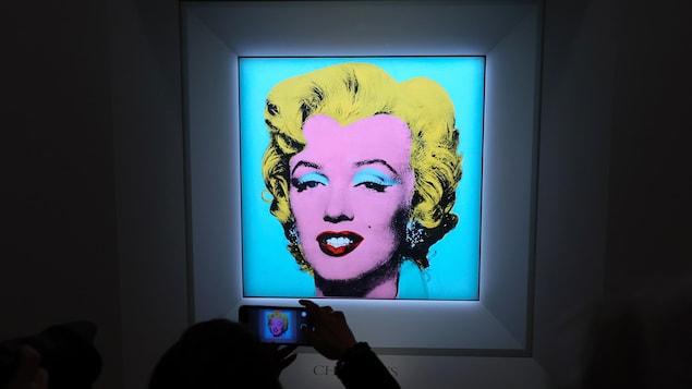 Une femme photographie avec son téléphone intelligent une peinture de Marilyn Monroe signée Andy warhol.