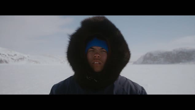 Un jeune homme portant un capuchon regarde devant lui dans un environnement arctique. 