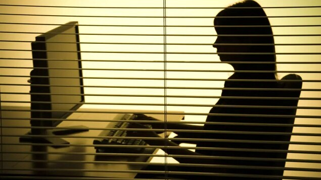 La silhouette d'une femme assise à un bureau. 