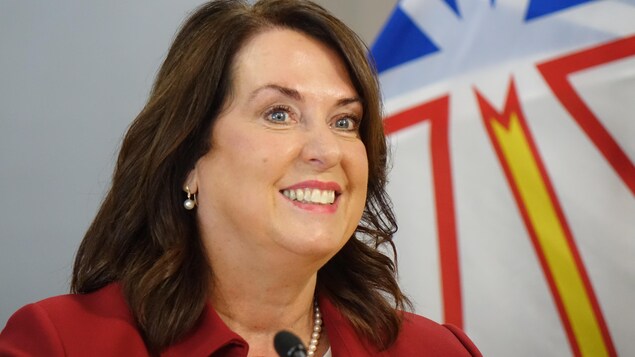 Siobhán Coady sourit, avec un drapeau de Terre-Neuve-et-Labrador derrière elle.