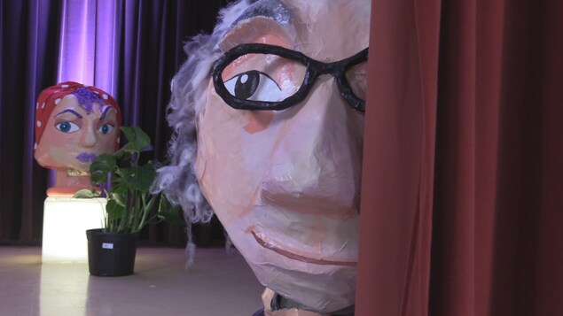 Une grosse tête en papier mâché d'un homme à lunettes.