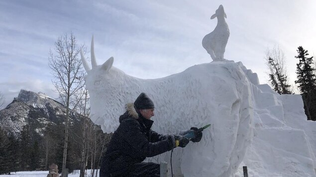 Un sculpteur travaille la neige pour donner l'apparence de fourrure à sa chèvre, fait de neige.