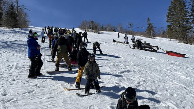 Des planchistes attendent en file en haut d'une montagne.