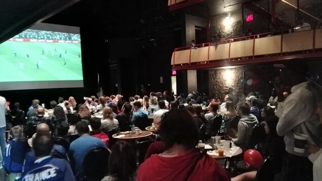 Des gens regardent le match diffusé sur écran géant dans une salle de spectacle. Des gens regardent le match diffusé sur écran géant dans une salle de spectacle.