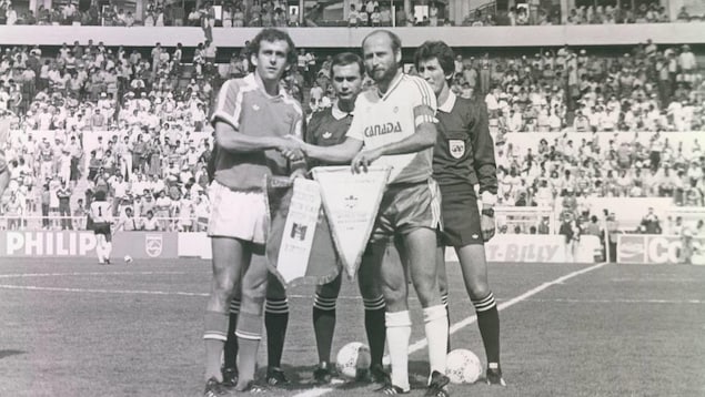 Photo en noir et blanc des capitaines des équipes de la France et du Canada qui se serrent la main et échangent les fanions avant la partie. Photo en noir et blanc des capitaines des équipes de la France et du Canada qui se serrent la main et échangent les fanions avant la partie.