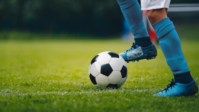Plan au dessous des genoux d'un joueur de soccer, qui a le pied sur un ballon.