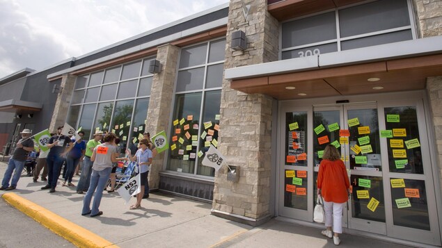 Une cliente se bute à des portes fermées devant un magasin de la SAQ pendant que des syndiqués en grève arborent des pancartes à Rosemère, en banlieue de Montréal Une cliente se bute à des portes fermées devant un magasin de la SAQ pendant que des syndiqués en grève arborent des pancartes à Rosemère, en banlieue de Montréal