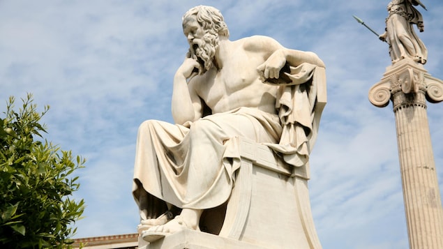 Vêtu d'une toge, Socrate est assis, pensif.