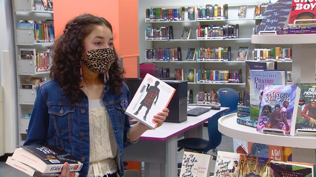 Une jeune fille tient une sélection de livres dans ses mains.