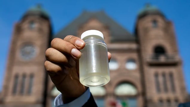 Un récipient transparent contenant de l'eau jaune brandit devant le bâtiment de l'Assemblée législative de l'Ontario.