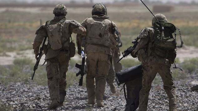 Trois militaires, vus de dos, marchent l'arme à la main. Trois militaires, vus de dos, marchent l'arme à la main.