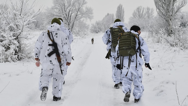 De soldats et un chien marchent dans un chemin ennneigé.