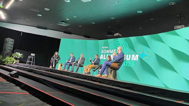 Des intervenants assis sur des chaises sur une scène au Sommet de l'aluminium.