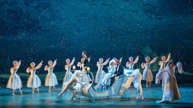 Un traineau blanc acceuille un homme et une femme qui sont entourés de danseurs célébrant la neige. Un traineau blanc acceuille un homme et une femme qui sont entourés de danseurs célébrant la neige.