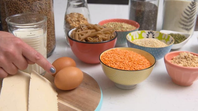 On voit du tofu, un verre de lait, deux oeurs et des bols contenant des lentilles et des céréales, disposés sur une table.