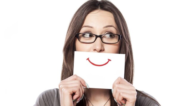 Femme tenant devant sa bouche un carton sur lequel il est dessiné un sourire.