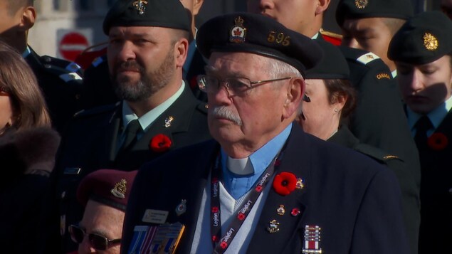 Un vétéran portant plusieurs médailles militaires est debout à l'extérieur lors d'une cérémonie du jour du Souvenir.