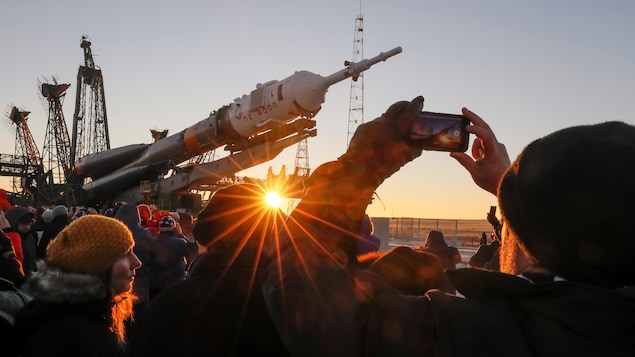 Des spectateurs regardent la fusée être installée sous le soleil levant.