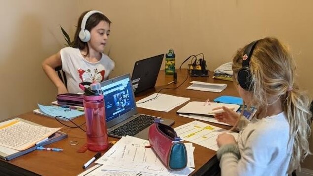 Deux fillettes à une table suivent chacune leur professeur sur leur ordinateur.