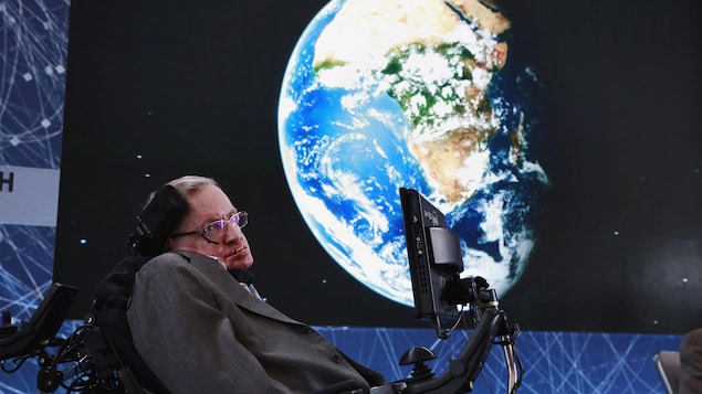 Stephen Hawking pose devant une image de la Terre.