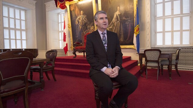 Stephen McNeil assis sur une chaise devant deux tableaux.