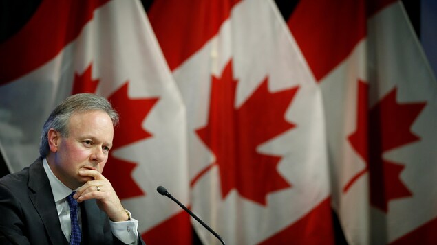 Stephen Poloz, la main sur le menton, devant trois drapeaux du Canada. Stephen Poloz, la main sur le menton, devant trois drapeaux du Canada.