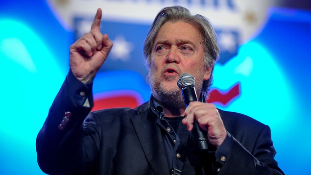 Steve Bannon prend la parole sur une scène, tenant un micro et levant le doigt. Steve Bannon prend la parole sur une scène, tenant un micro et levant le doigt.