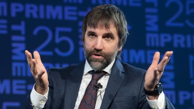 Le ministre prend la parole. Il est assis et porte un micro-cravate.