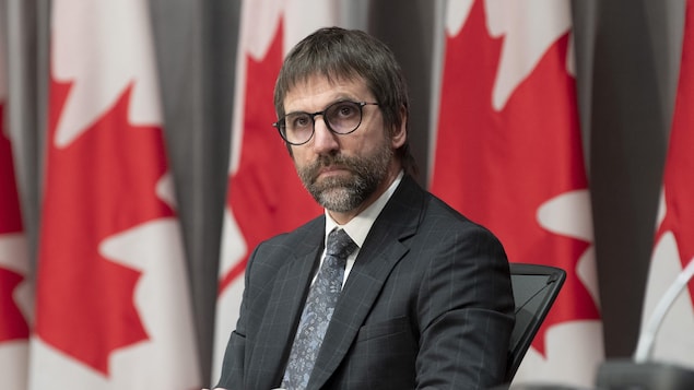 Steven Guilbault devant une rangée de drapeaux canadiens.