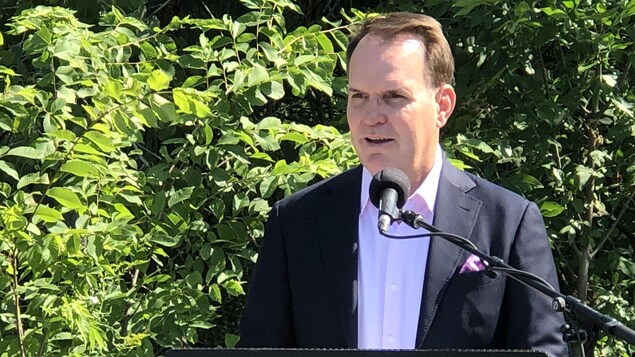 Le député MacKinnon pendant une conférence de presse devant des arbres.