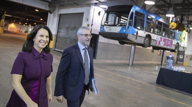 La mairesse de Montréal, Valérie Plante, et le directeur général de la STM, Luc Tremblay, avec, en arrière-plan, un autobus suspendu.