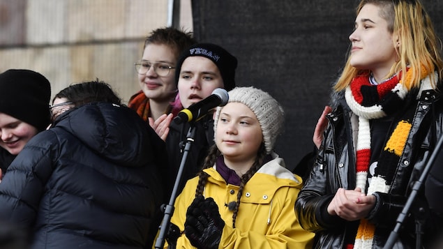 La militante Greta Thunberg devant un micro et des manifestants.