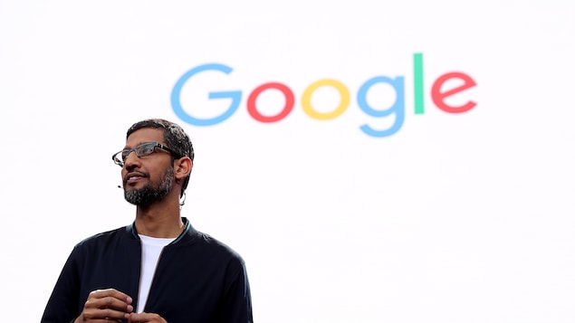 Le PDG de Google Sundar Pichai parle à une foule devant un écran orné du logo de Google. 