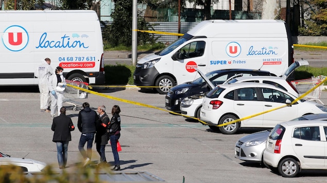 Des enquêteurs fouillent une voiture blanche dans le stationnement d'un supermarché. Des enquêteurs fouillent une voiture blanche dans le stationnement d'un supermarché.