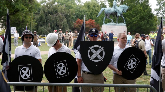 Quatre hommes habillent en blanc tiennent des bouclier noirs avec l'insigne de Vanguard America. Quatre hommes habillent en blanc tiennent des bouclier noirs avec l'insigne de Vanguard America.