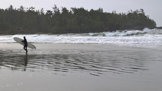 Un surfeur marche sur la plage avec sa planche sous le bras après être sorti de l'eau à Tofino, en Colombie-Britannique.