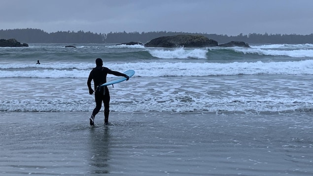 Un surfeur tient sa planche sous son bras pendant qu'il marche sur la plage en direction des vagues.