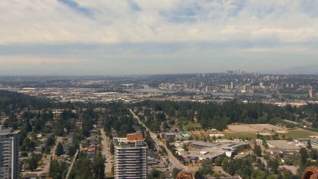 Grand plan de la région de Vancouver pris du haut d'un immeuble de Surrey avec des tours de bureaux, une partie du fleuve Fraser et un quartier résidentiel.