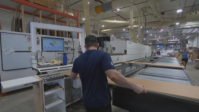 Un homme manipule une grande planche de bois.