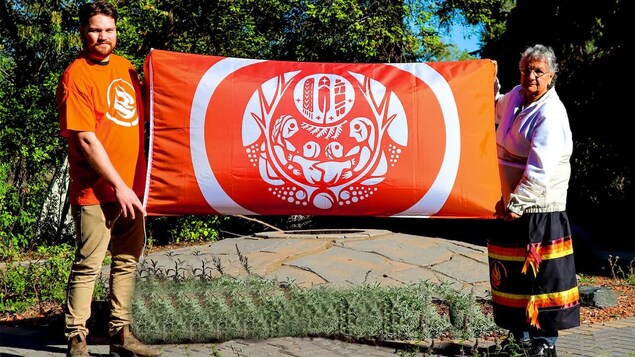 The survivor's flag features nine elements that were chosen in consultation with over 30 residential school survivors. Two people are holding the survivors' flag.