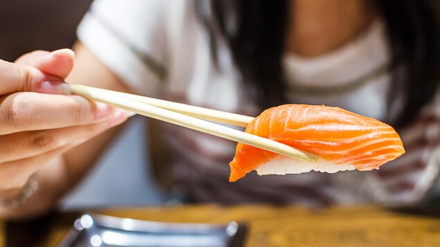 Une femme tient un sushi avec des baguettes. Une femme tient un sushi avec des baguettes.