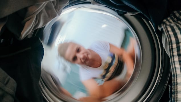Une femme observe sa lessive tourner dans la laveuse.