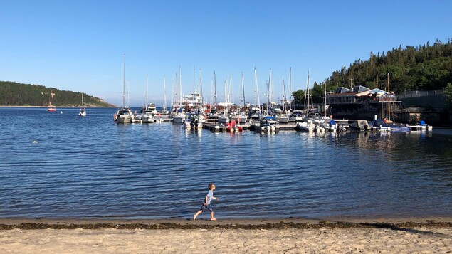 Des bateaux sur l'eau et un enfant qui court sur la plage