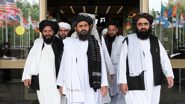 Un groupe d'hommes barbus et portant le turban sortent d'un bâtiment.