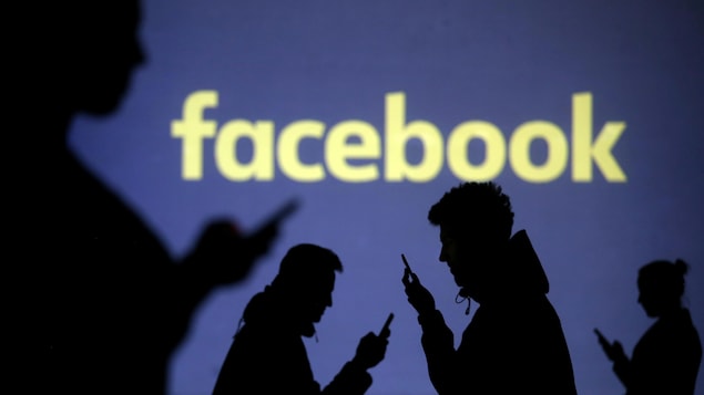 Des silhouettes d'utilisateurs de téléphones intelligents devant le logo de Facebook.
