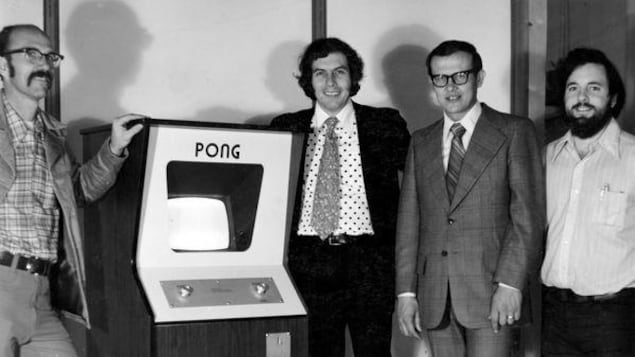 Ted Dabney pose à côté d'un jeu Pong. 