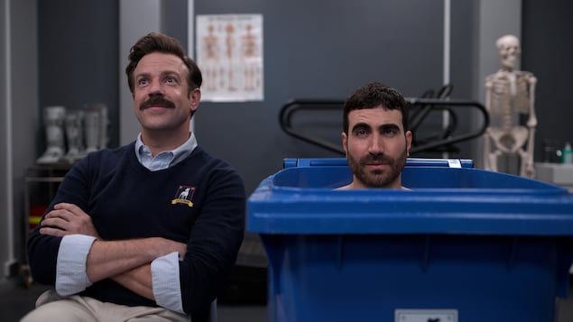 Deux hommes sont assis, dont l'un dans un bac de recyclage.